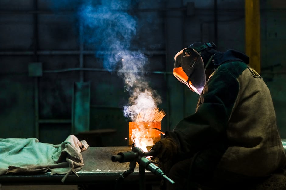 Welder working in an industrial workshop with sparks and smoke.
